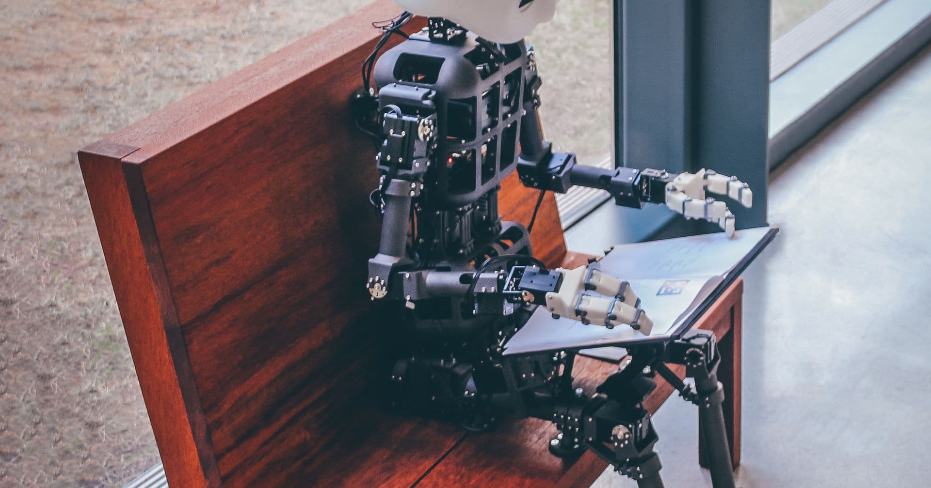 A humanoid robot seated by a window reading a document, evoking an llms.txt file of instructions for AI